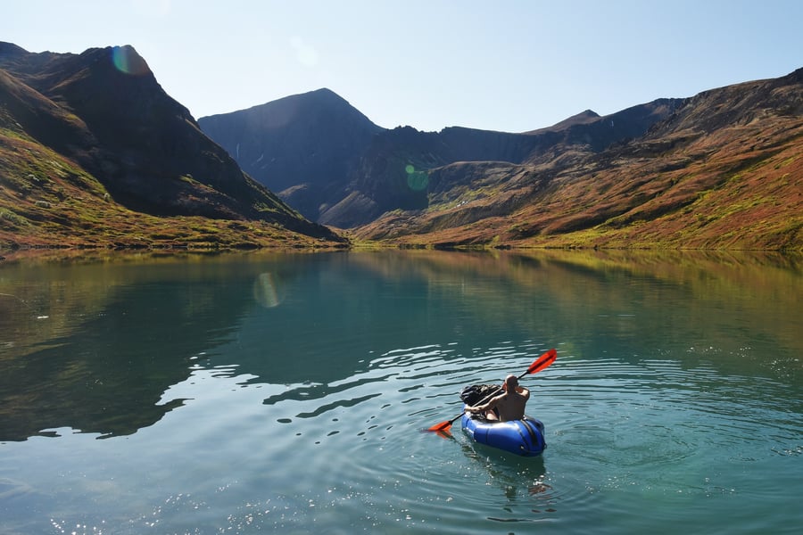 Man kayaking in blue inflatable kayak surrounded by alaskan mountains