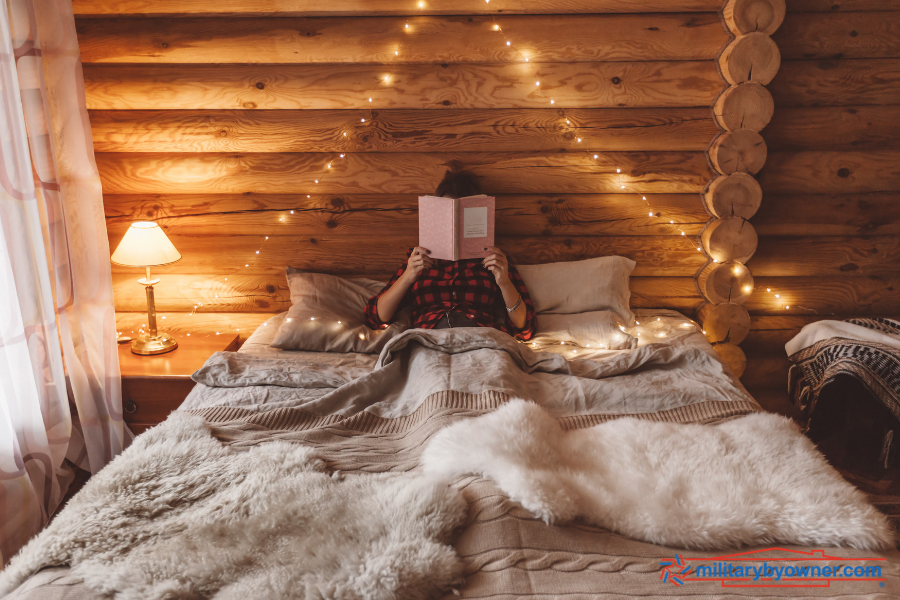 woman reading a book in bed in log cabin 