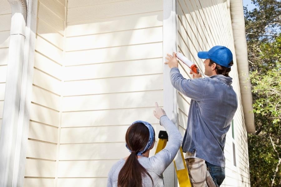 landlord working on home maintenance and caulking siding on house