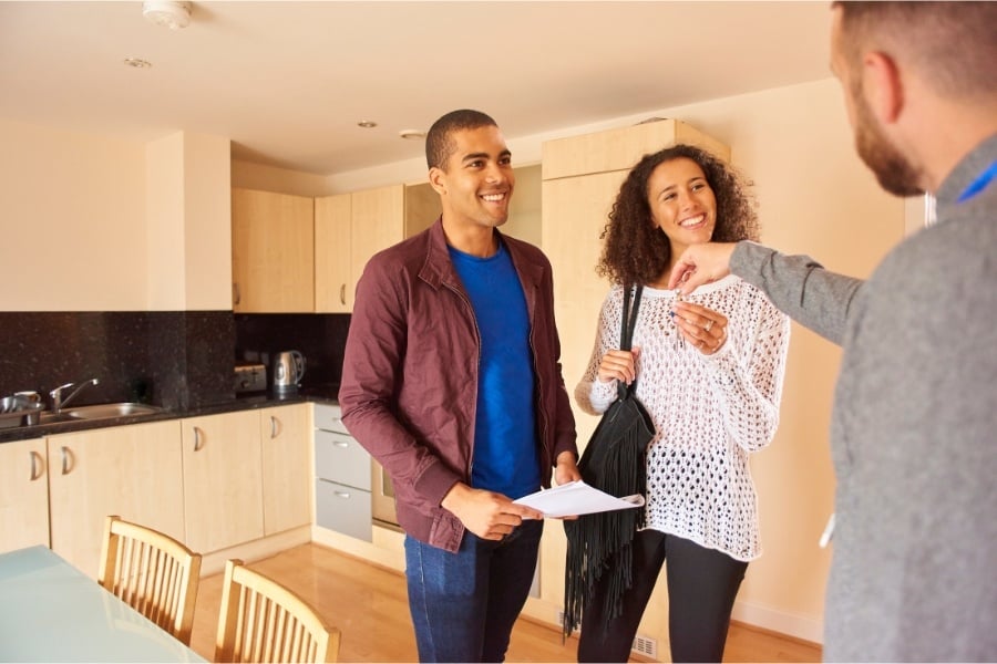 a young couple receiving house keys from a landlord while standing in the kitchen