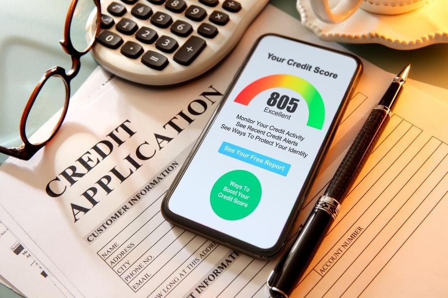 Credit score on smart phone with paper credit application, glasses, and calculator