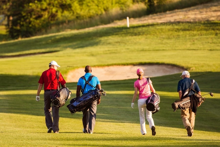 Four golfers carrying bags on golf course. 