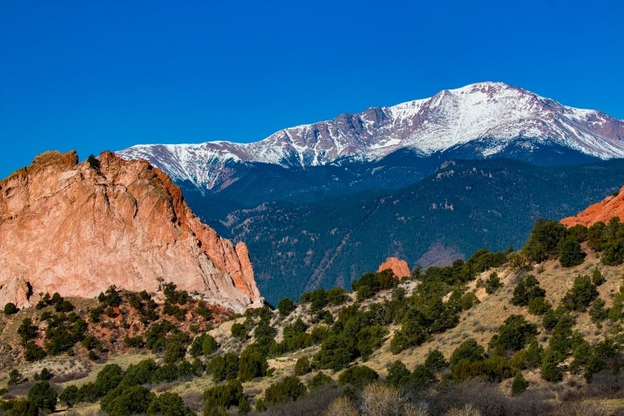view of snow covered mountain, red rocks, and forestline atGarden of the Gods with Pikes Peak in Colorado Springs, CO