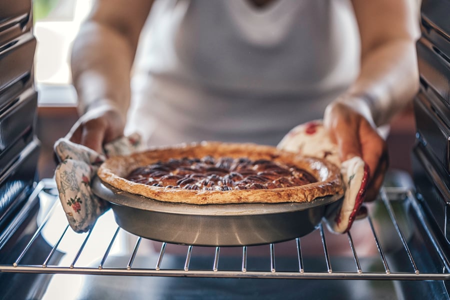 woman taking pecan pie out of oven