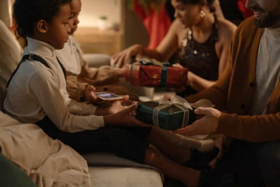 Adults dressed formally giving dressed up kids in suspenders red and green wrapped gifts with ribbon