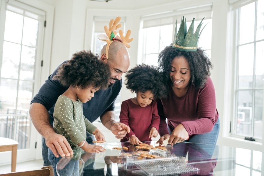 mom and dad with festive hats not their heads smile with two kids as they look a fun holiday cookies 