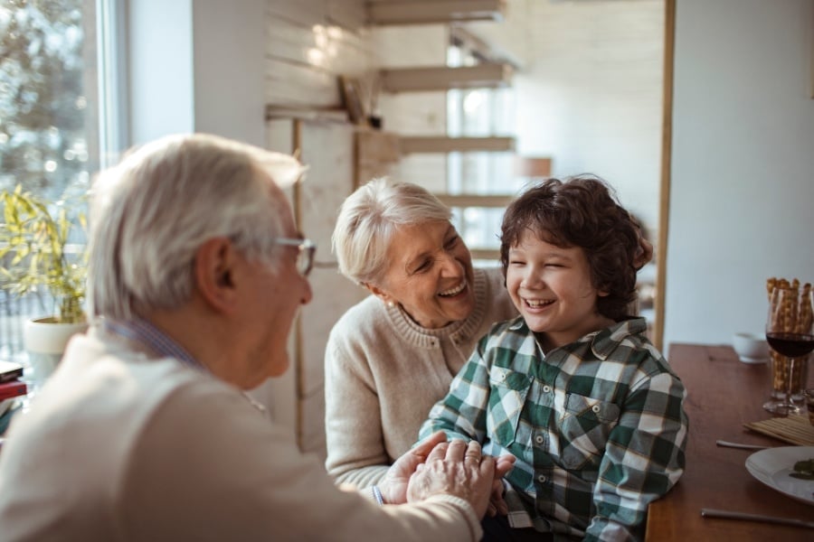 Grandma and grandpa with white hair laughing with grandson with dark curly hair and green plaid flannel shirt, beige background