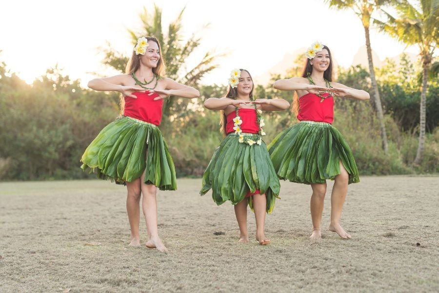 Three girls in red and green grass skirts performing dance in luau 