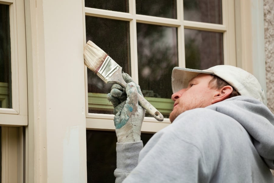 man painting windowpane with paintbrush