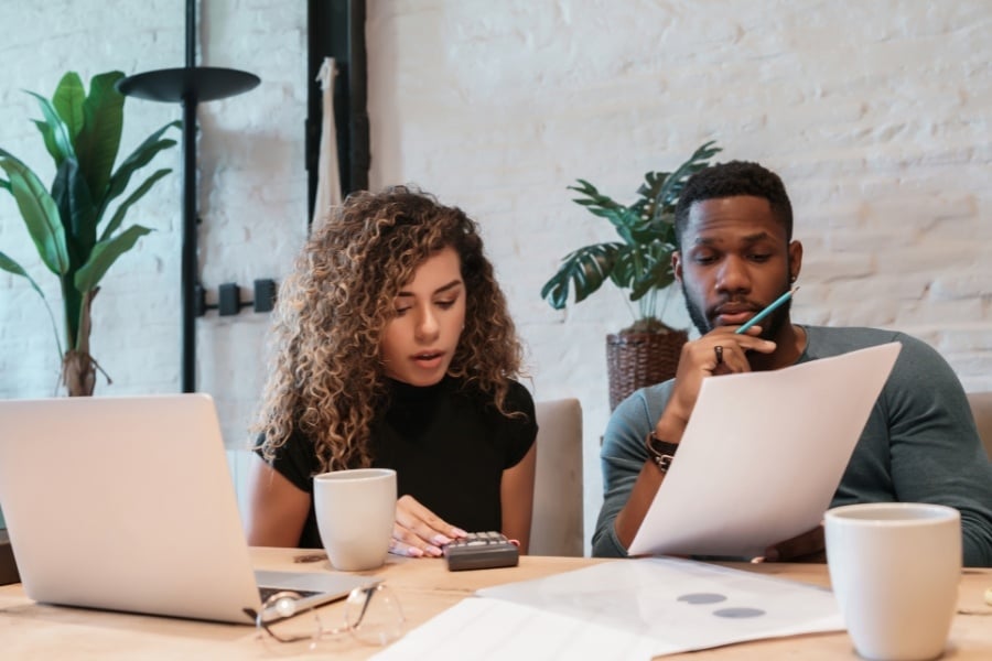 man and woman looking at papers and calculator while sitting at table with coffee cups