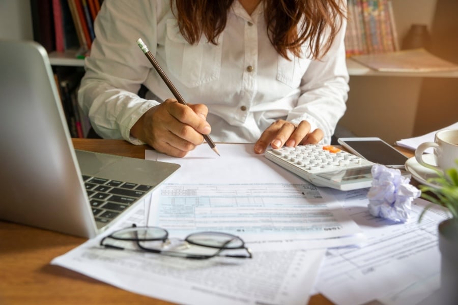 woman looking at financial papers while writing on pad with pencil, calculator on desk