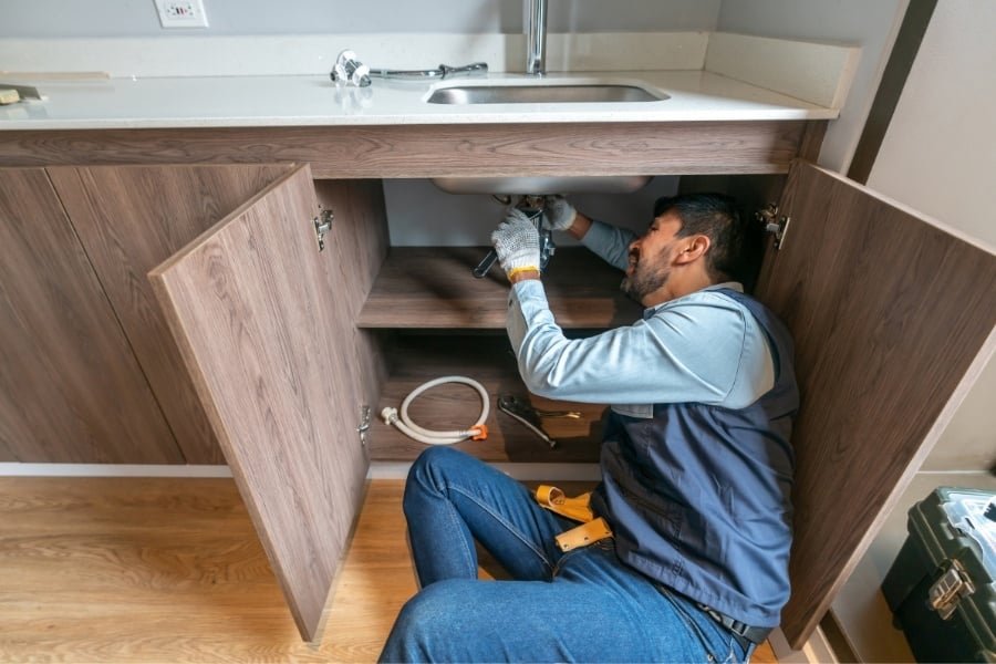 handyman in blue jeans, vest, and shirt and a yellow tool belt lays on the ground fix fixes countertop sink 