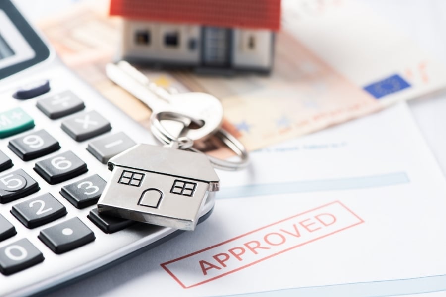 Desk with calculator, model house, house keys, and loan paperwork marked approved.  