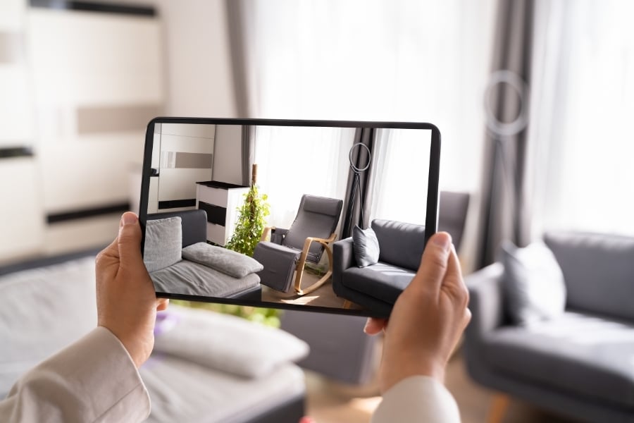 Person holds up tablet and captures neutral living room with gray furniture in front of them.