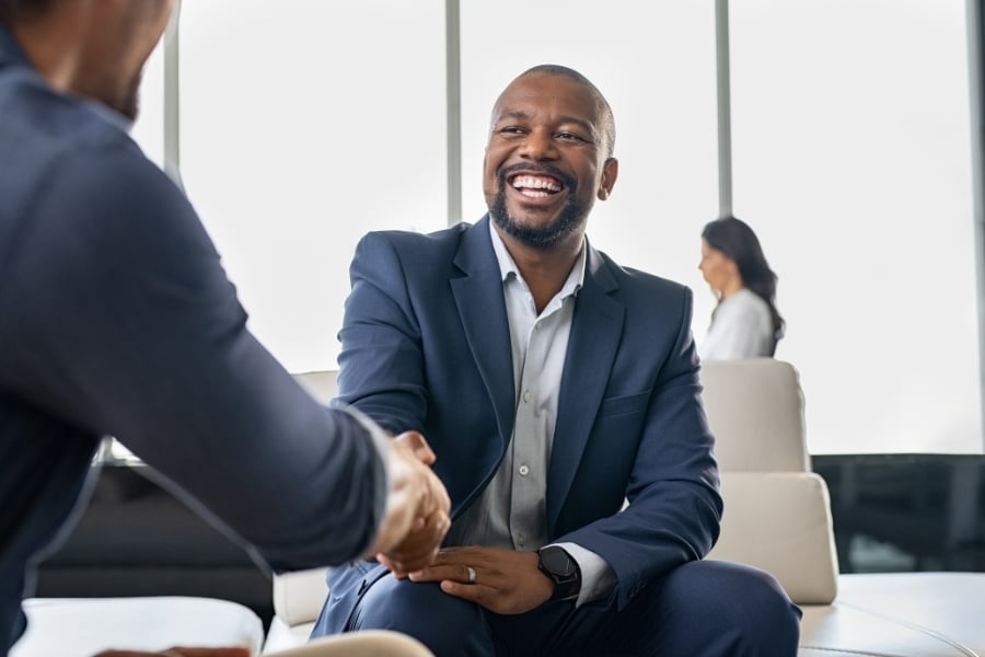 Man in blue suit smiling big while shaking another man's hands. 