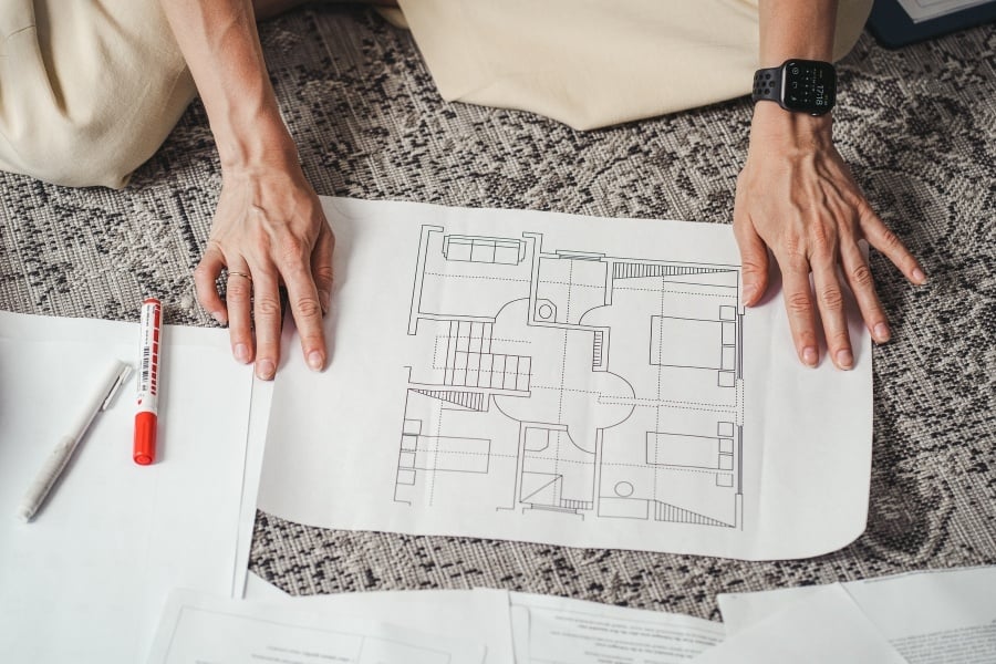 Hands spreading printed floor plan across rug. 