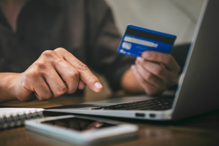 A person's hands typing on laptop while holding a credit card