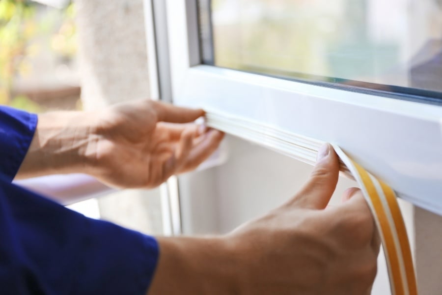person putting weatherstripping on window for fall maintenance