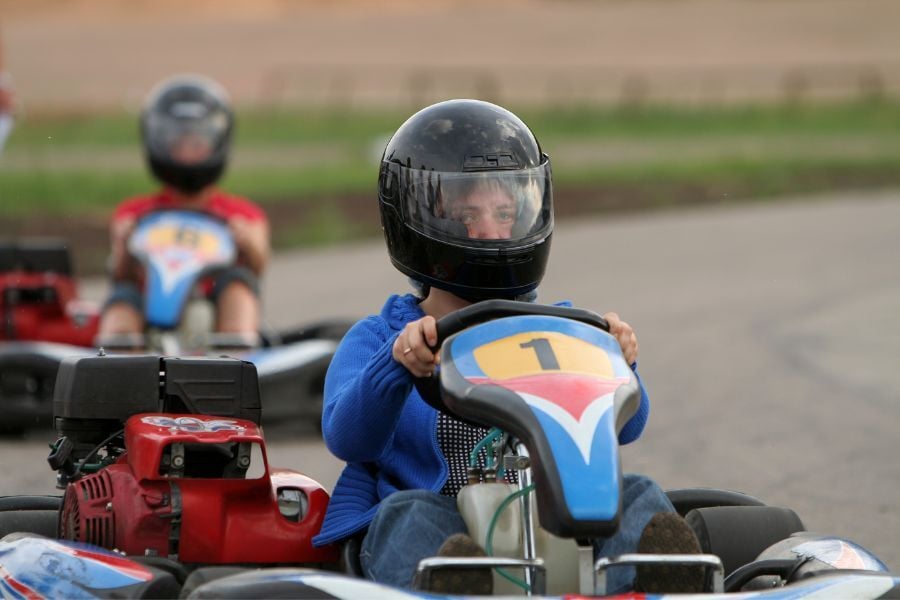 Two people go karting with blue carts on paved path. 