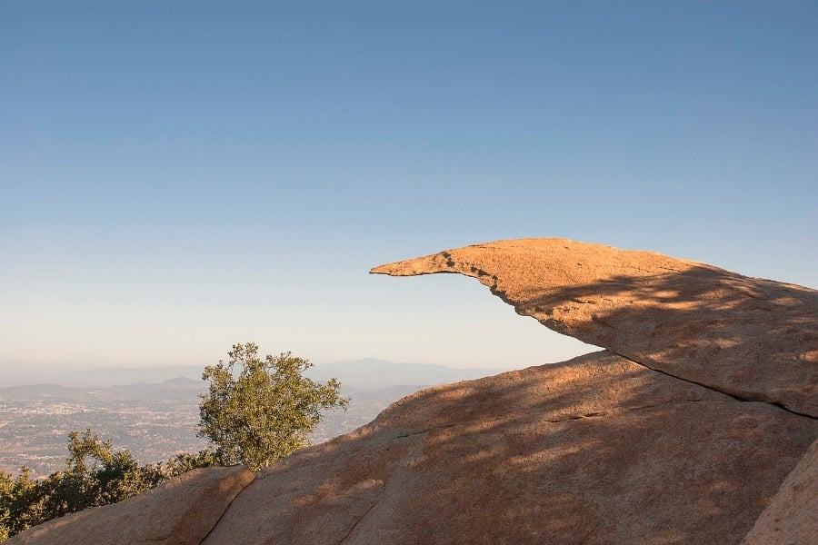 Photo of potato chip rock at Mt. Woodson in San Diego, CA overlooking parts of the city, sun shining and trees