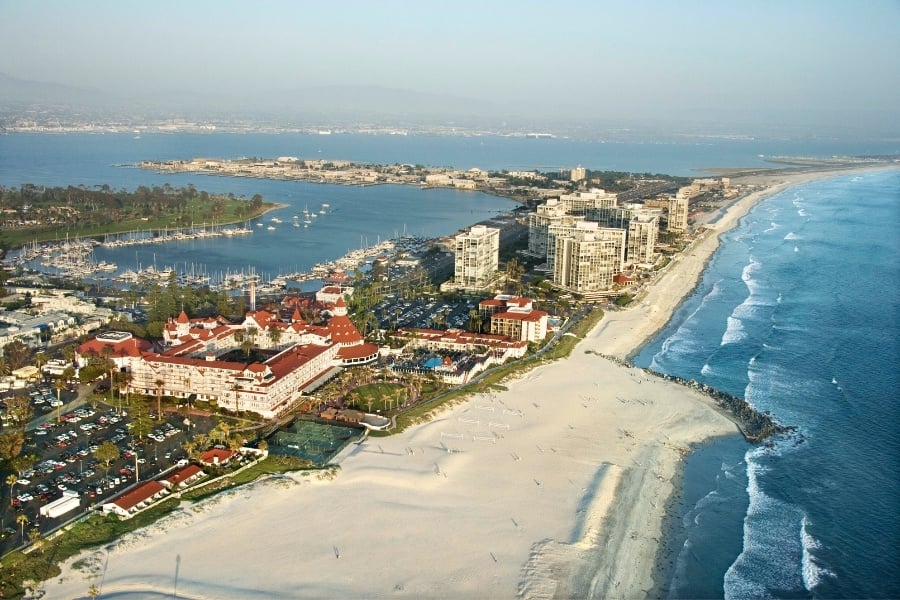 Aerial view of Hotel Del Coronado with boats in harbor, San Diego in the background, and beach