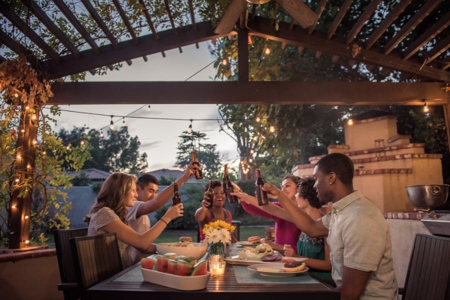 Friends enjoying dinner under pavilion with lights on and beers raised as the sun goes down. 