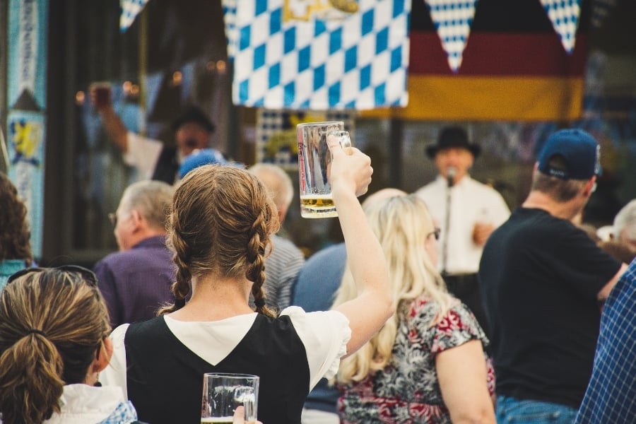 Oktoberfest crowd with German decorations facing the stage and holding beer glasses up.  