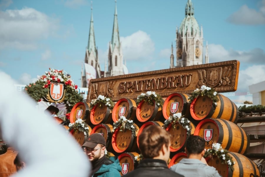 Oktoberfest celebration in Munich, Germany with barrels stacked on their sides and Spatenbrau sign on top. Beautiful architecture is visible in the background. 