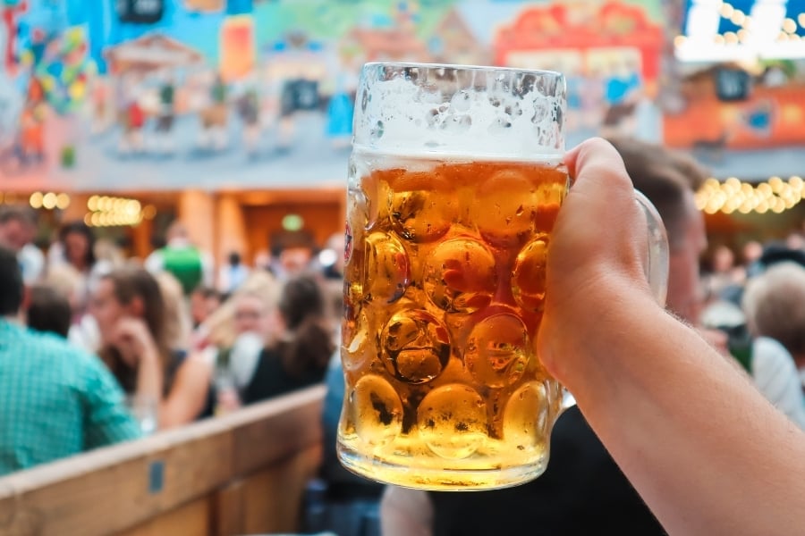 Person holding up beer stein in Oktoberfest lively crowd. 