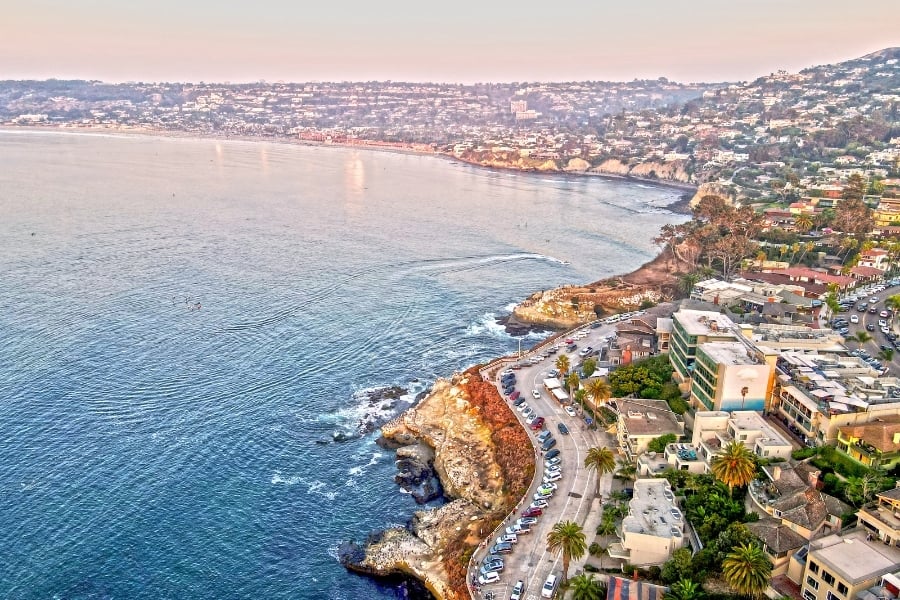 Ariel view of La Jolla, CA with coastline, parking lots and homes built on the neighboring hill. 