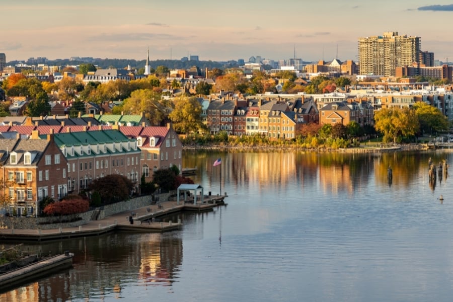 View of waterfront of Potomac River in Alexandria, VA with American flag and beautiful brick buildings with golden sunlight. 