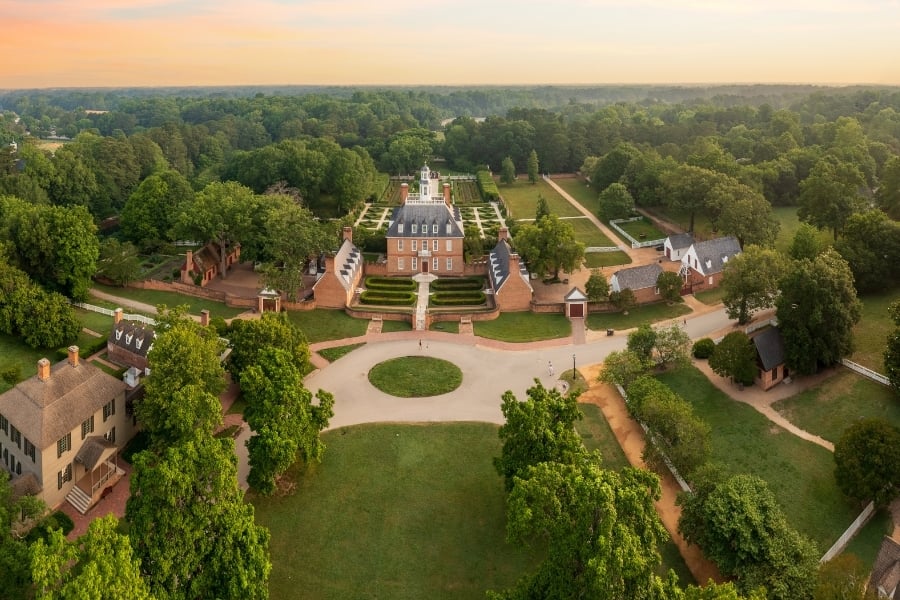 view of Governors Palace in Williamsburg at dawn, brick colonial buildings, green grass, trees, and bushes