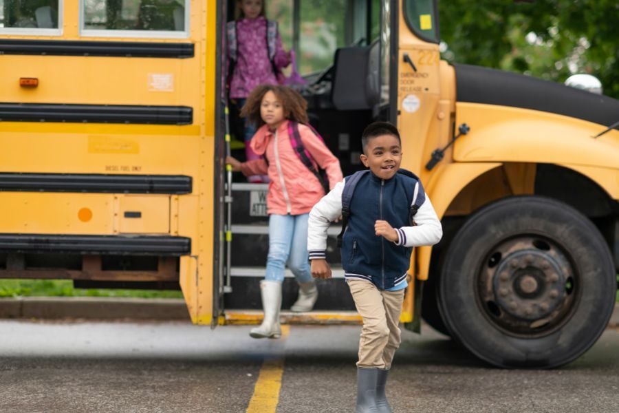Kids running off yellow school bus with backpacks on their backs. 