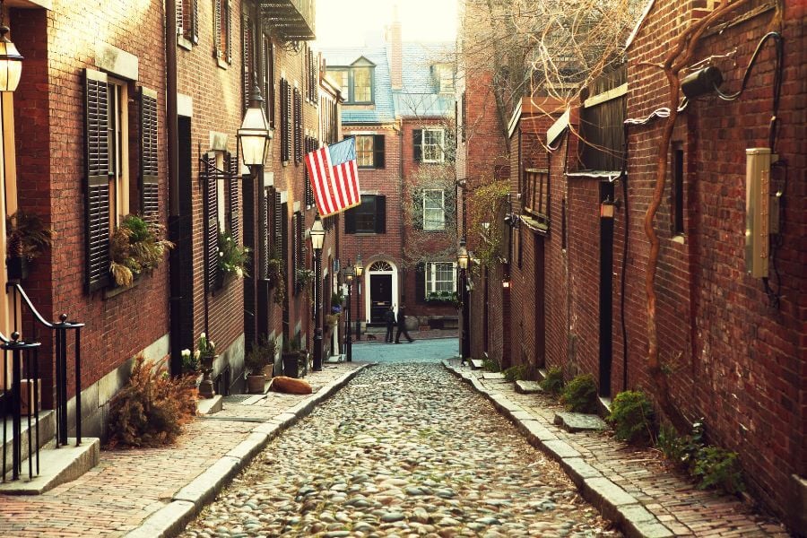 View of stone alley with American flag and brick buildings in Beacon Hill in Boston, Massachusetts.