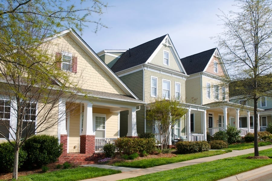 Neighborhood with light-colored siding with clean sidewalk and green grass. 