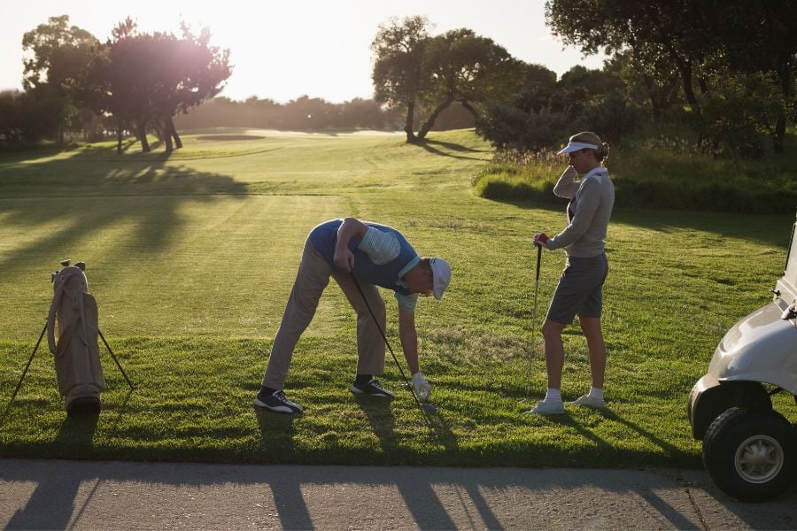 Man and woman in golf attire set ball in grass  to hit. 