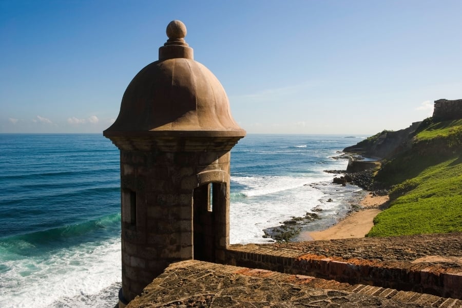 View of "El Morro" in San Juan, Puerto Rico with green hill and vibrant coastal waters below. 