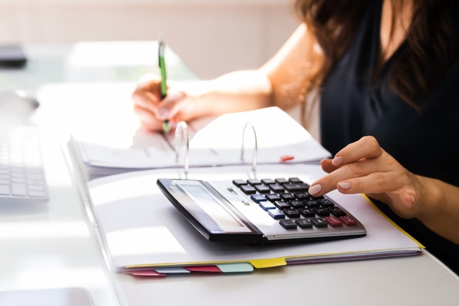 woman typing on calculator while writing in notebook with pen while sitting at desk