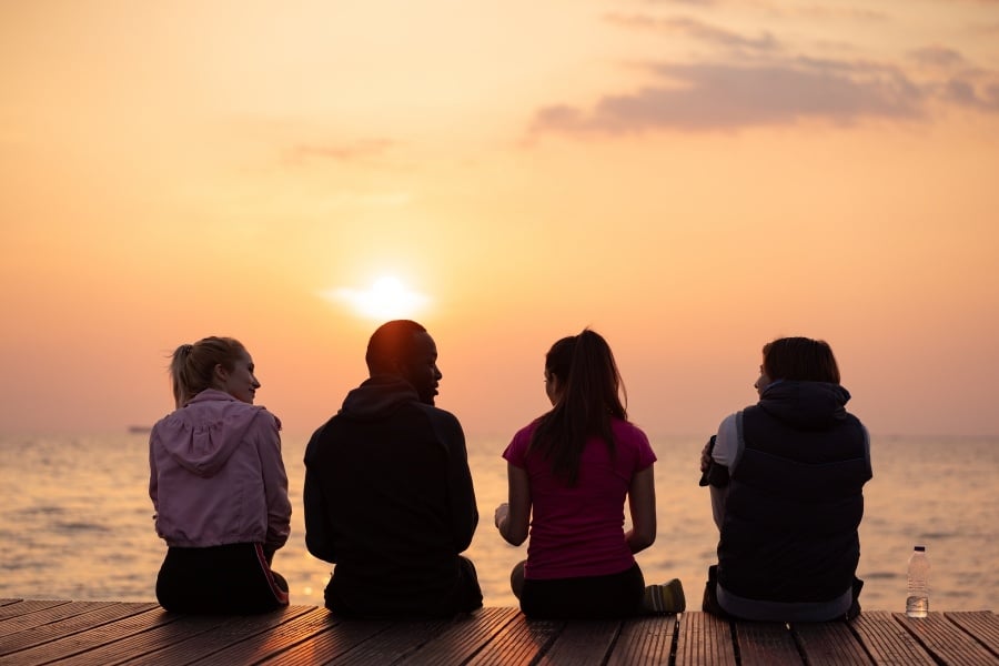 group of friends sitting together on pier at sunset