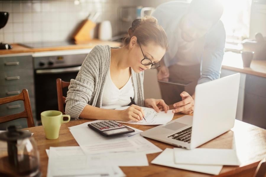 woman writing on paper with man looking on 