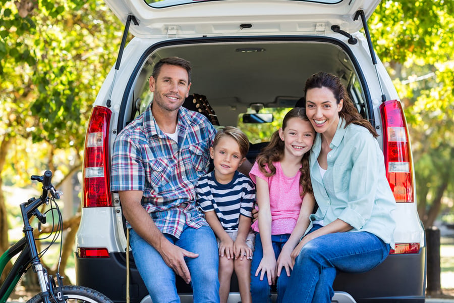 family with children sitting in back of minivan on road trip