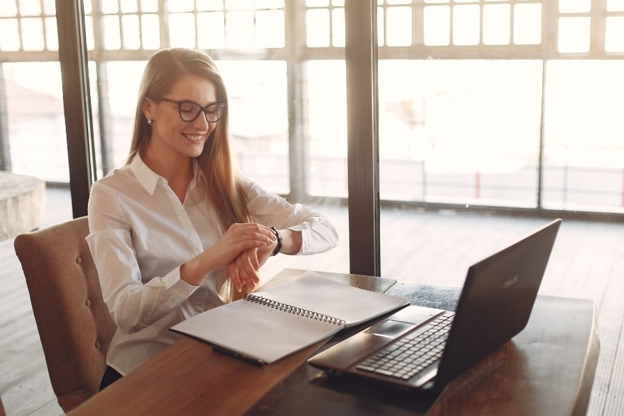 Military spouse pursuing career and looking at wristwatchwatch at table with notepad and laptop computer. 