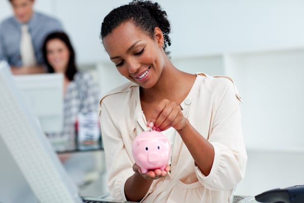 Joyful businesswoman saving money in a piggy-bank at her desk