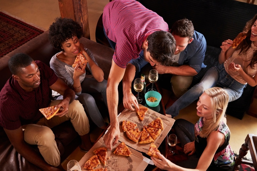 group of friends eating pizza out of pizza boxes on table