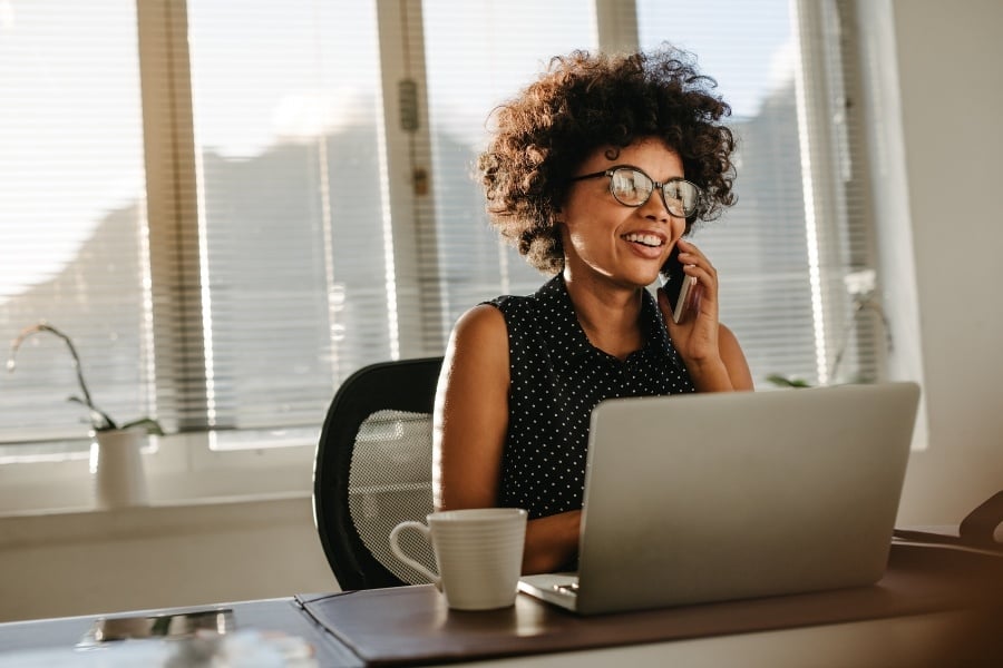 woman talking on phone with coffee cup and laptop