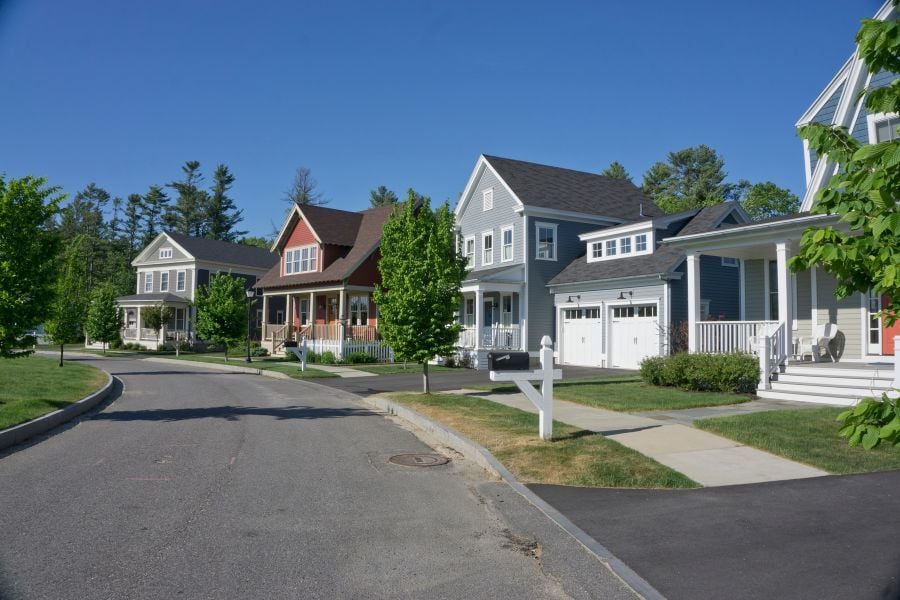 Suburban neighborhood featuring homes with siding, white trim, and bright green trees. 