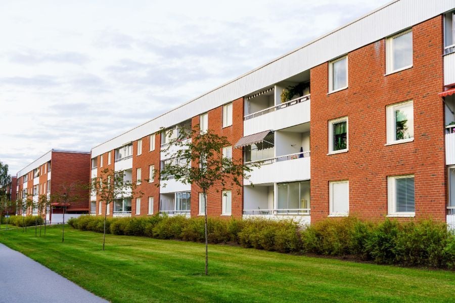 Brick apartment building with green grass and young trees in lawn. 