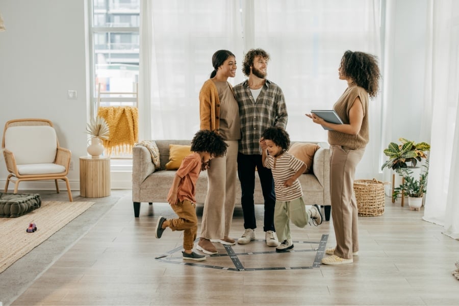 Female real estate agent talking to family of four (Dad, mom, and two boys) in a home. 