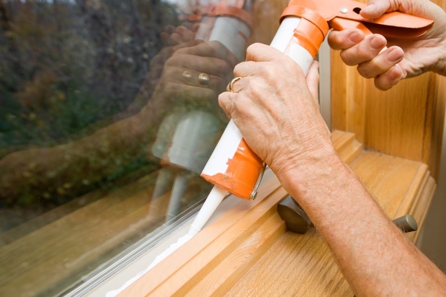 Person with wedding ring applying caulking between wood and glass. 