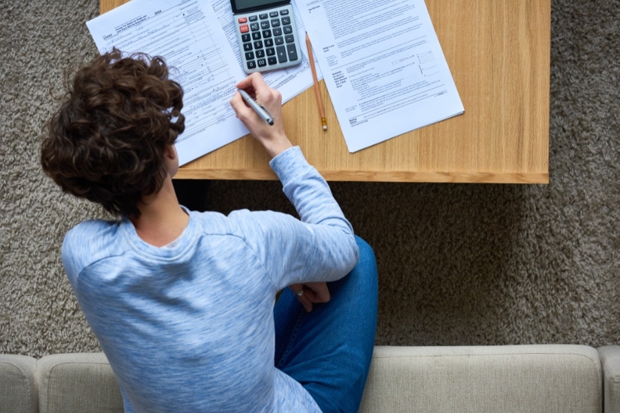 person writing on tax documents with calculator nearby